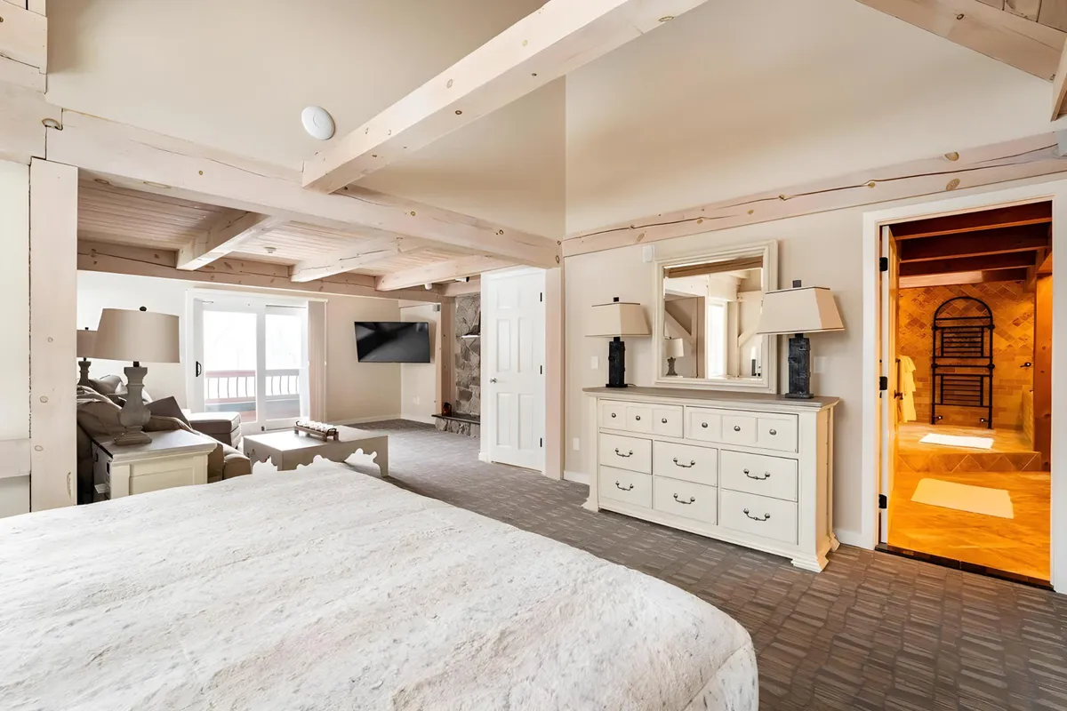 A spacious bedroom with a king-size bed, dresser with lamps, television, and double doors opening to a private balcony. Daylight streams in, suggesting a fresh mountain morning, and the balcony hints at a direct connection to the outdoors—perfect for enjoying serene mountain air in privacy.