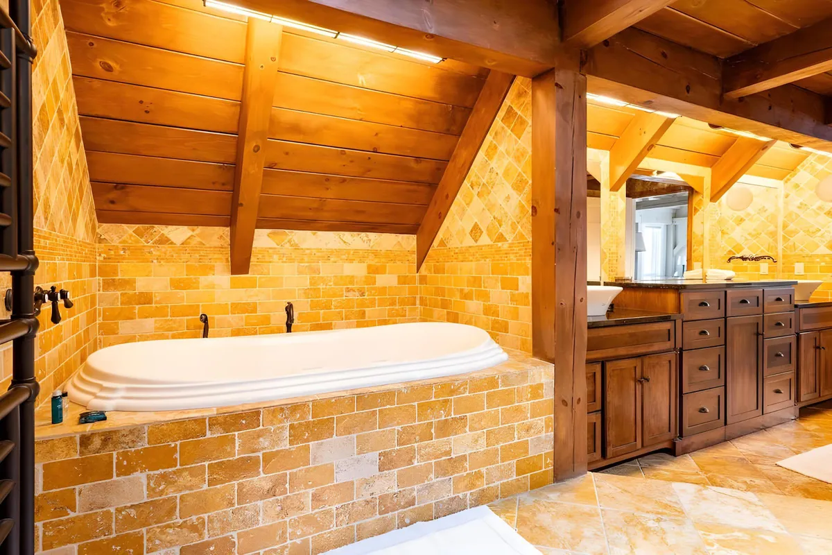 A luxurious bathroom interior featuring a freestanding soaking bathtub, rich wooden cabinetry, and textured stone walls, exuding a tranquil spa-like ambiance. The design encourages relaxation and self-care after an active day.