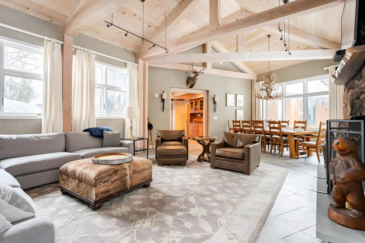 A large sectional sofa in an open-plan living and dining space, accented by a decorative bear statue and exposed wooden beams. The area is designed for family gatherings, relaxation, and entertaining, with a warm, inviting atmosphere.
