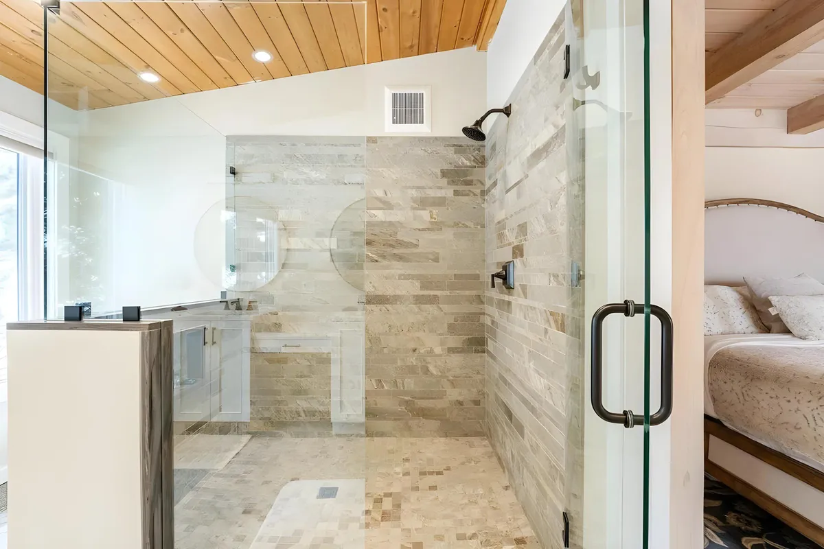 An elegant bathroom with a glass-enclosed shower, natural stone wall, wooden ceiling, and a spacious vanity area. Sunlight streams into the room, enhancing the fresh and rejuvenating mood that invites restorative self-care.