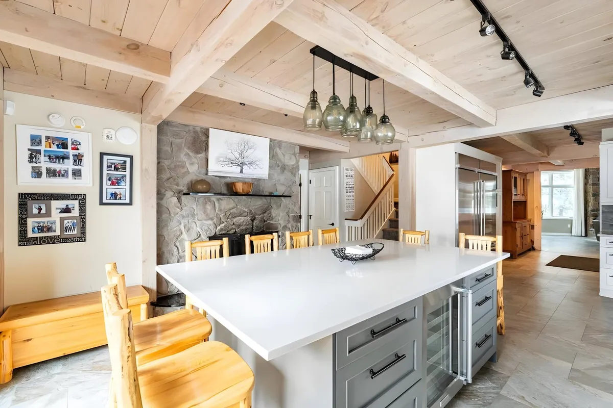A chef’s kitchen featuring a large kitchen island, wooden chairs, and artful stone wall décor. The space is designed for cooking, socializing, and entertaining groups, with ample space for meal preparation and casual conversation.