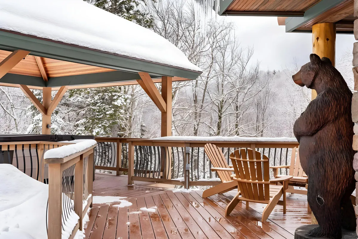 The image features a snow-covered landscape with a rustic wooden deck and a gazebo, complete with Adirondack chairs and a playful bear sculpture. The setting exudes tranquility and invites relaxation after a day on the slopes, while the open view hints at the proximity to ski trails and mountain scenery.