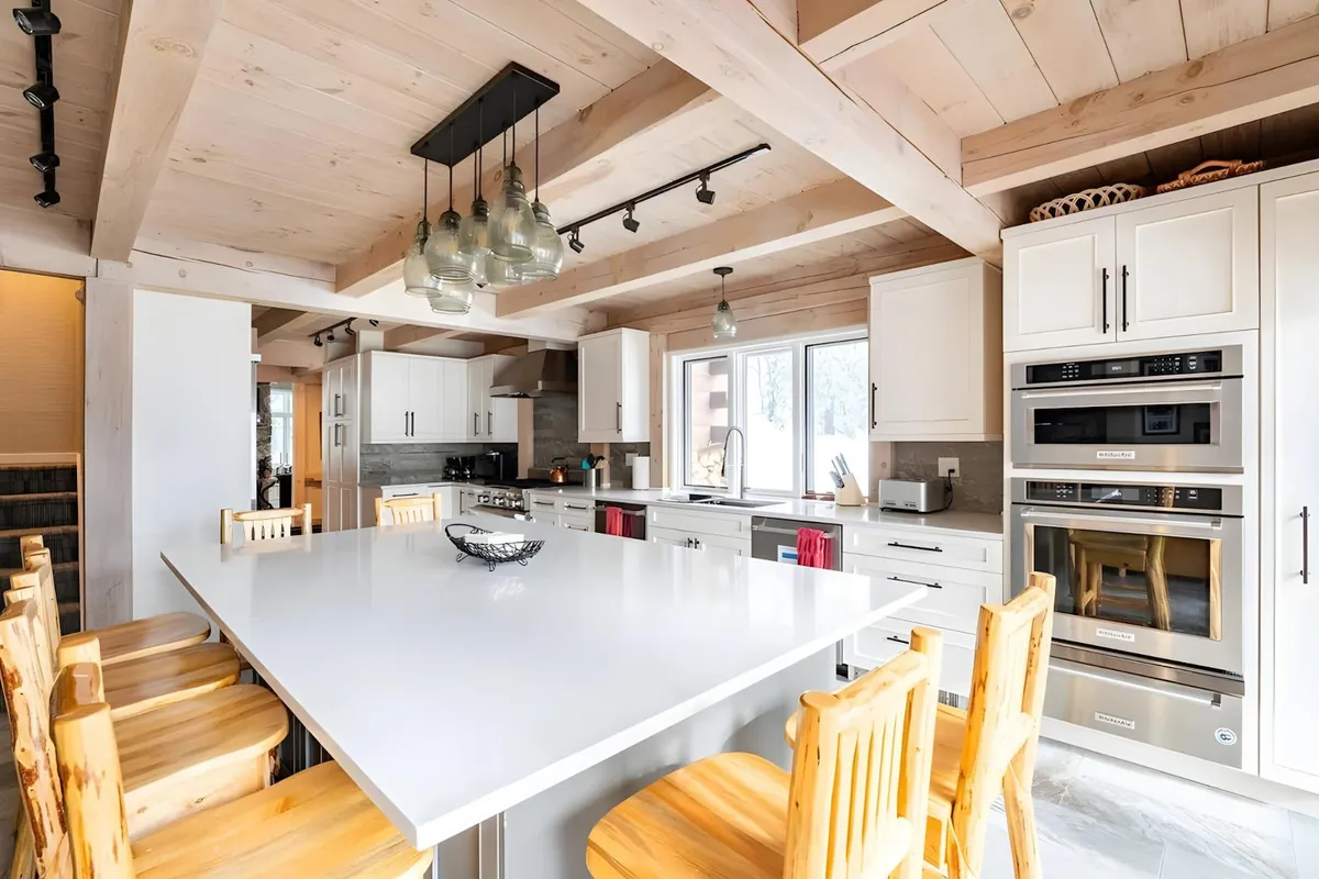 A modern, open kitchen with a large kitchen island, wooden bar stools, and state-of-the-art appliances. The space is designed for both cooking and socializing, with high-end finishes and a welcoming, communal layout.
