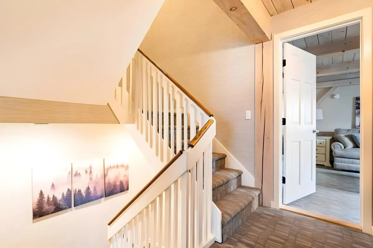 An inviting view of a staircase with wall art and an open door leading to another room, evoking a sense of arrival and transition between spaces. The open, airy design and subtle touches of art and décor hint at both individuality and ease of movement.