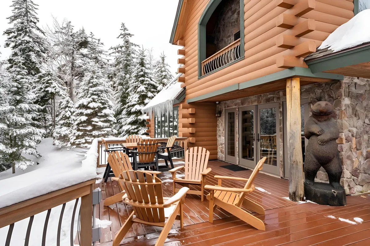 A tranquil setting featuring a wooden deck, bear statue, and comfortable seating surrounded by snow-covered trees. The outdoor area invites guests to unwind and enjoy the beauty of the landscape.