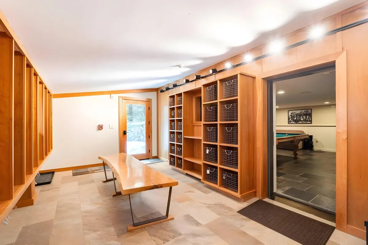 A mudroom area featuring a wooden bench, shelving units with baskets for organization, and a door leading to another part of the home. The setting evokes warmth, practicality, and a well-organized space—perfect for changing out of ski gear after a day on the slopes or prepping for outdoor excursions with pets or family.