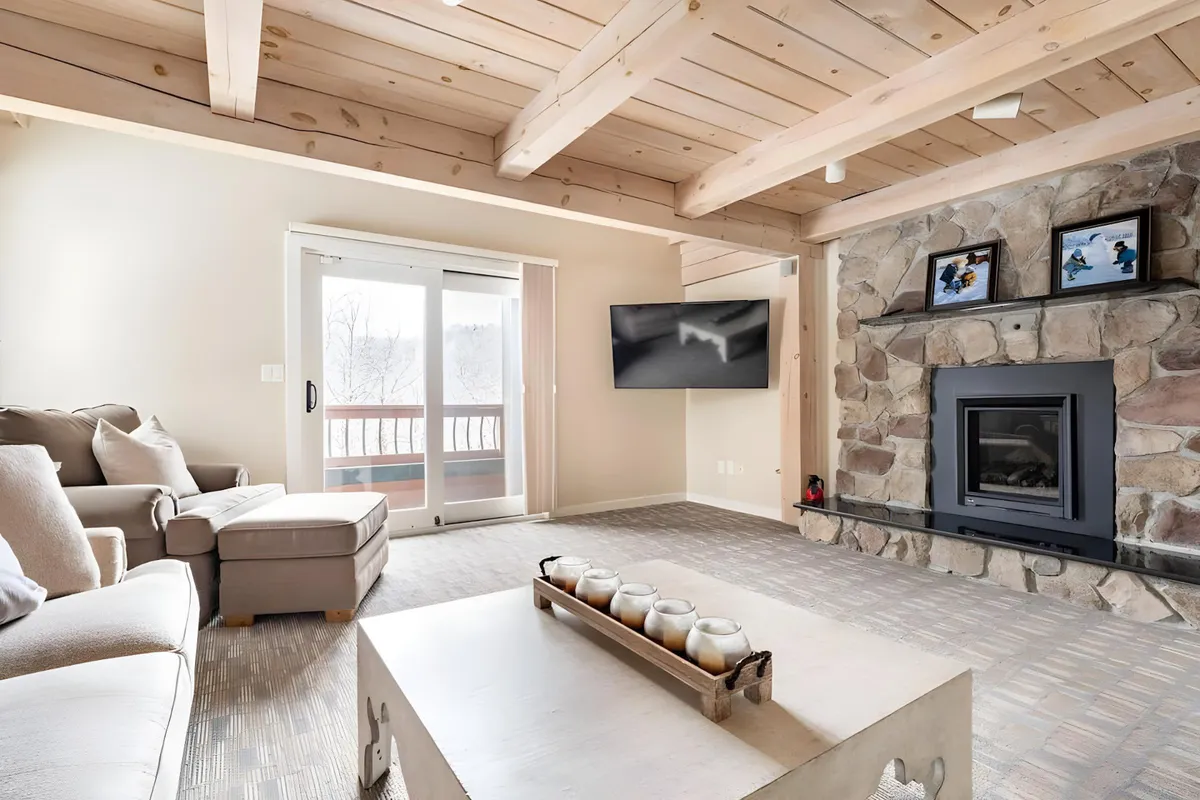 A cozy lounge area with a stone fireplace, comfortable seating, and large sliding doors leading to a balcony. The space invites relaxation by the fire while also offering access to fresh air and stunning outdoor views.